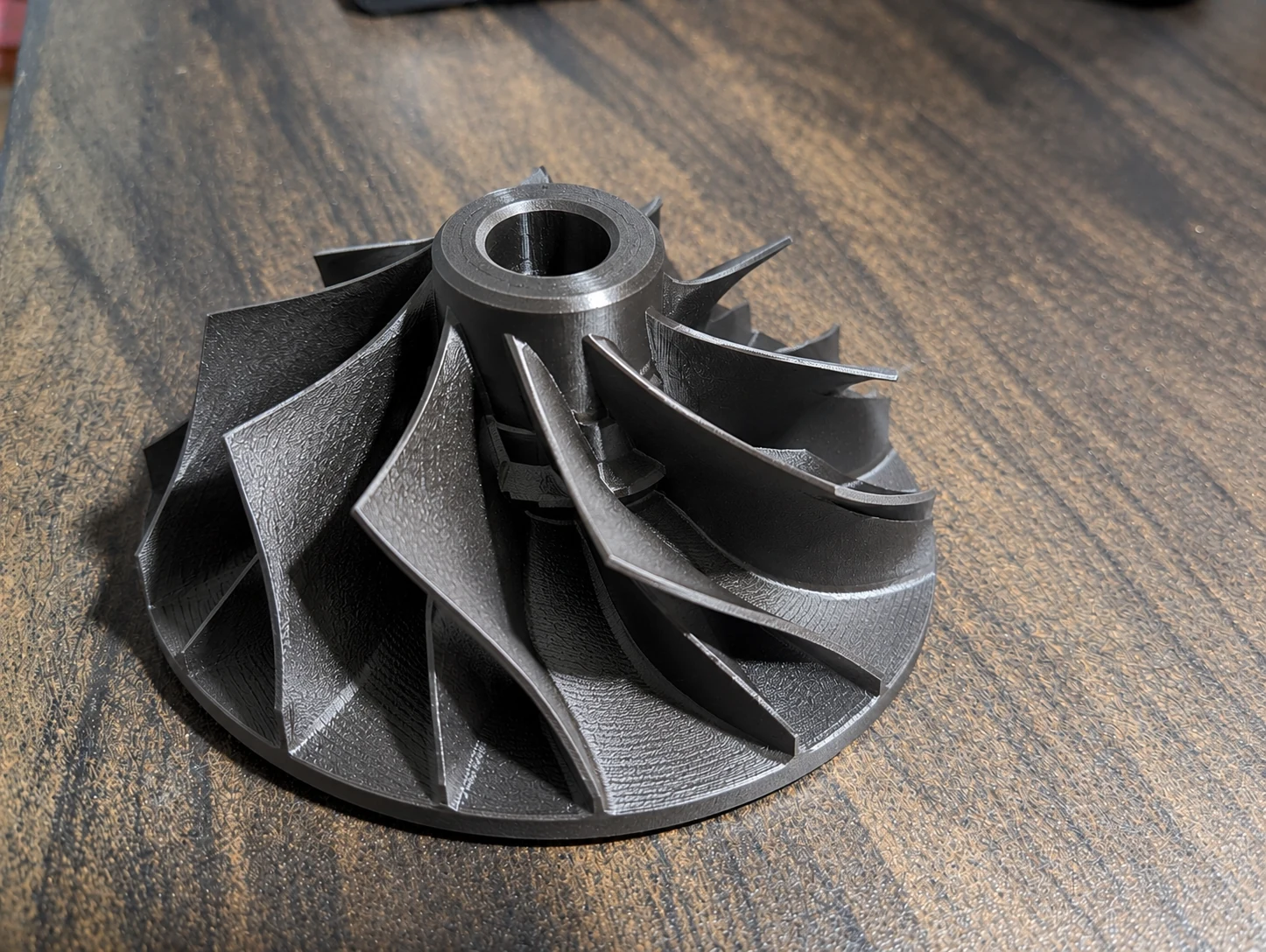 Black 3D-printed impeller with curved blades and a central bore on a workbench