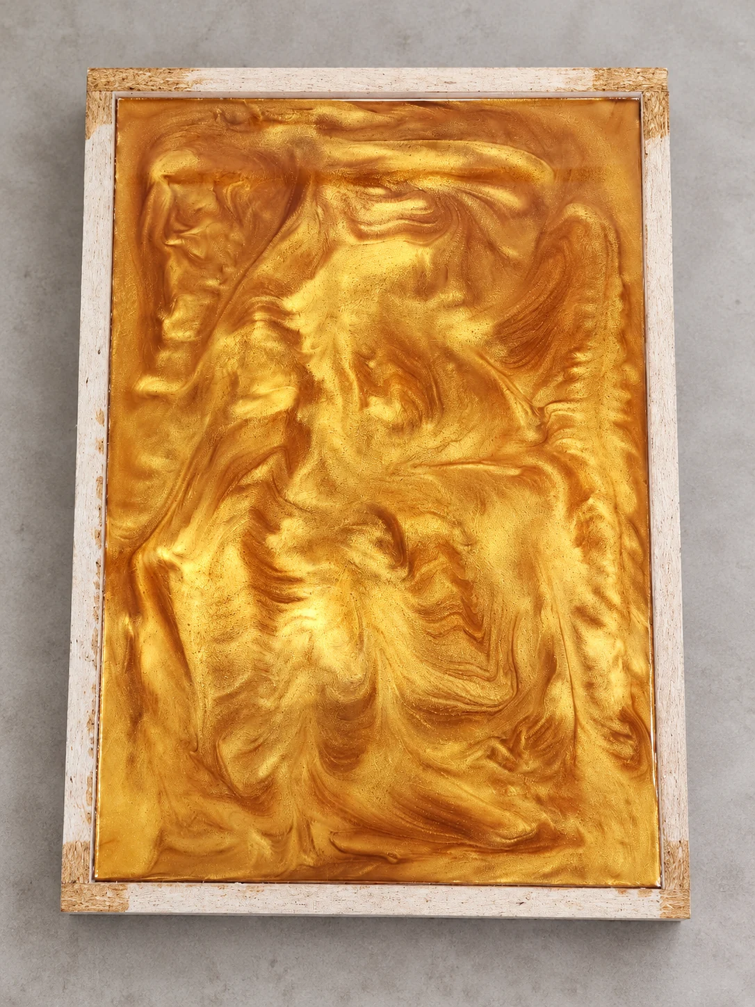 Stage 1 gold-pigmented epoxy panel with swirling patterns in its rectangular casting frame